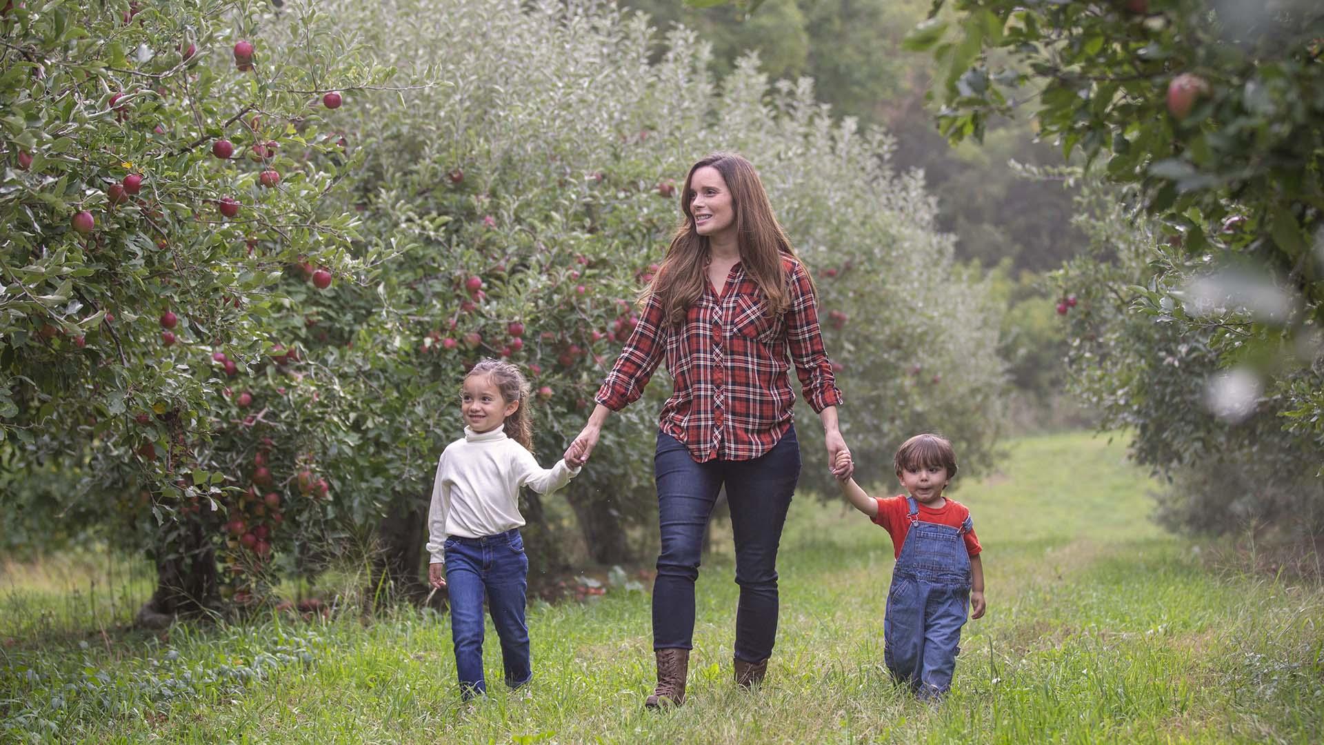 An adult and two children walking in an orchard.