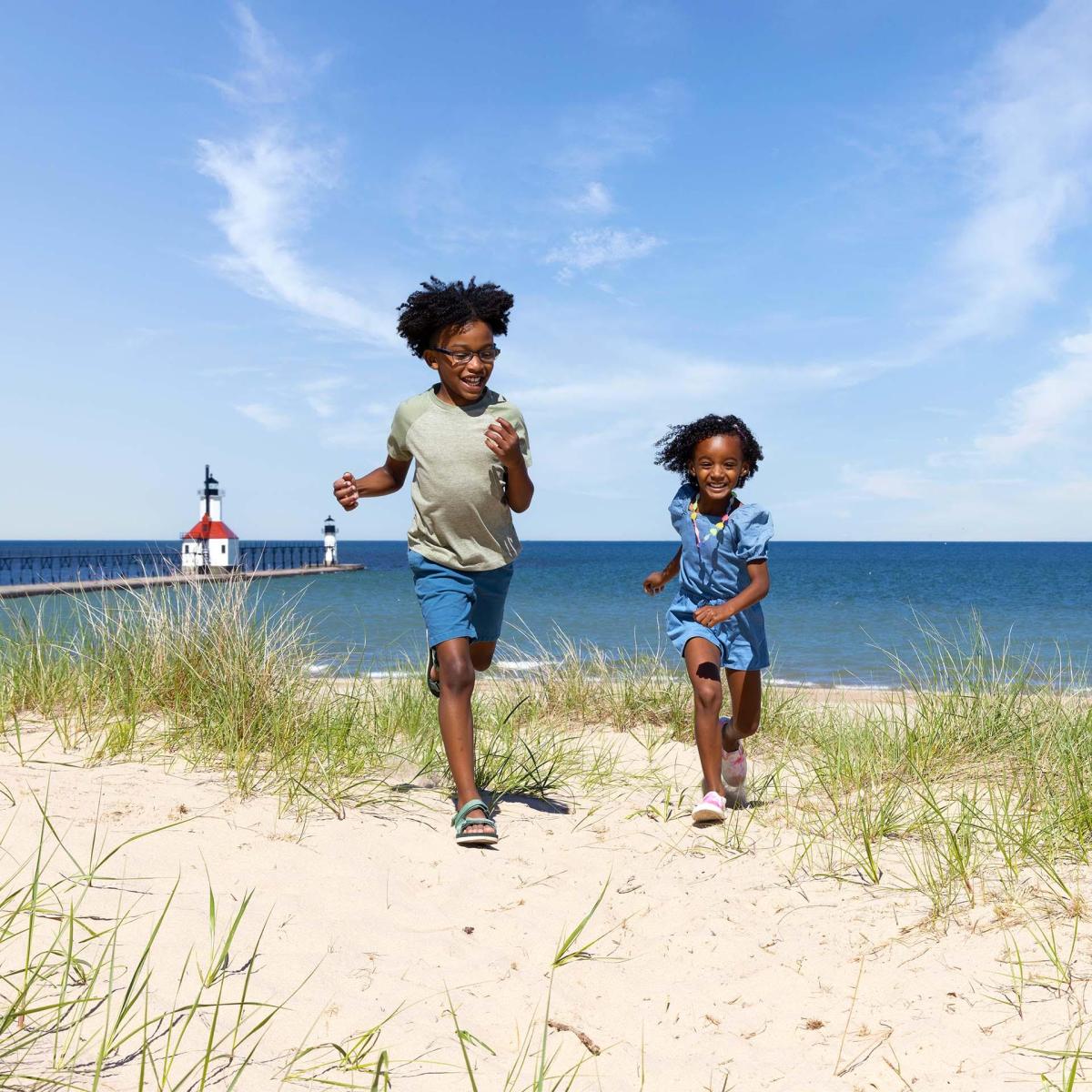 Kids running on the beach with the St. Joseph lighthouse in the distance.