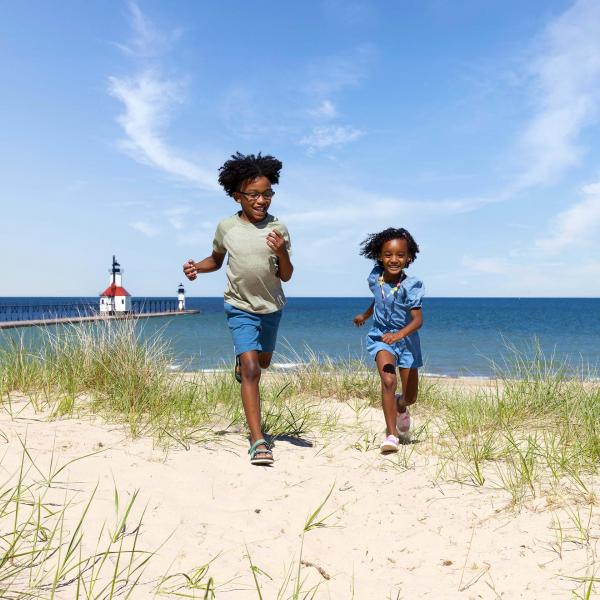 Kids running on the beach with the St. Joseph lighthouse in the distance.