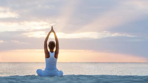 A woman practicing yoga on the beach during a warm sunrise, with soft golden light illuminating the peaceful morning scene