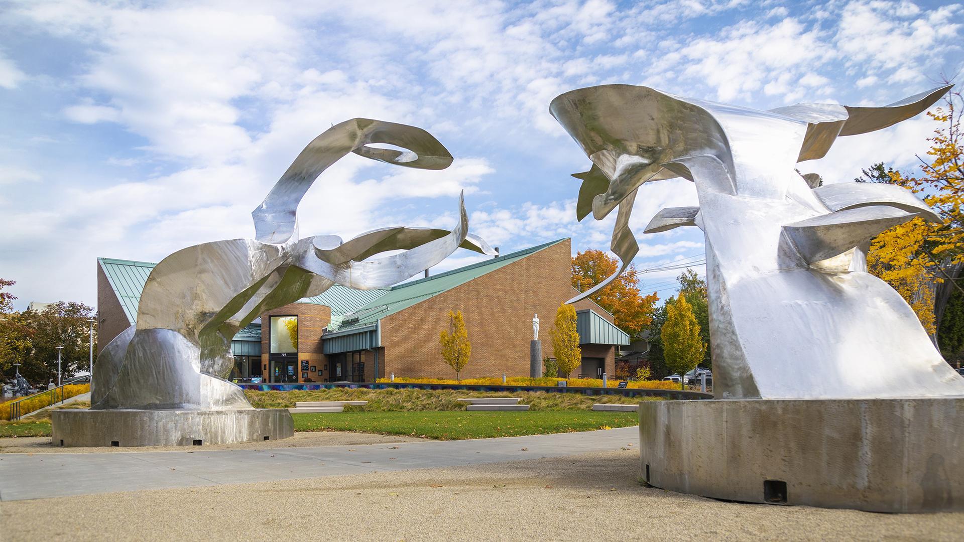 An image of the exterior of the Krasl Art Center, with two large outdoor sculptures by Richard Hunt displayed at the corner of the property and the entrance to the art center visible in the background