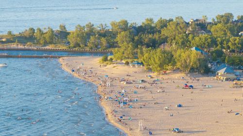 A drone shot of Silver Beach on a sunny summer day, with groups of people scattered along the shore enjoying the beach, swimming, and relaxing in the sun
