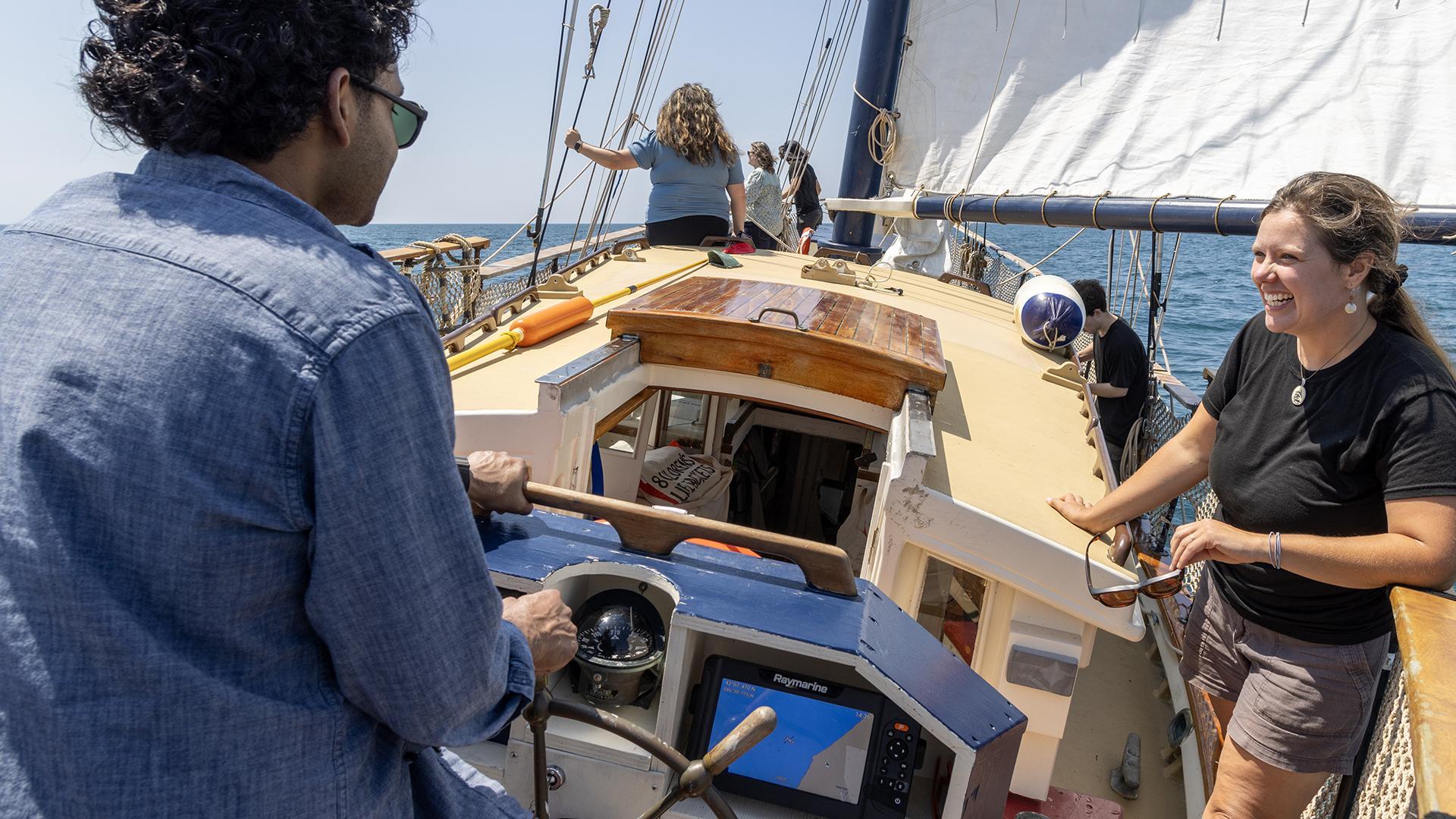 A man sailing a historic ship on Lake Michigan during a clear summer day, with blue skies and calm water stretching to the horizon. The ship's wooden details and sails are visible, capturing a classic maritime scene