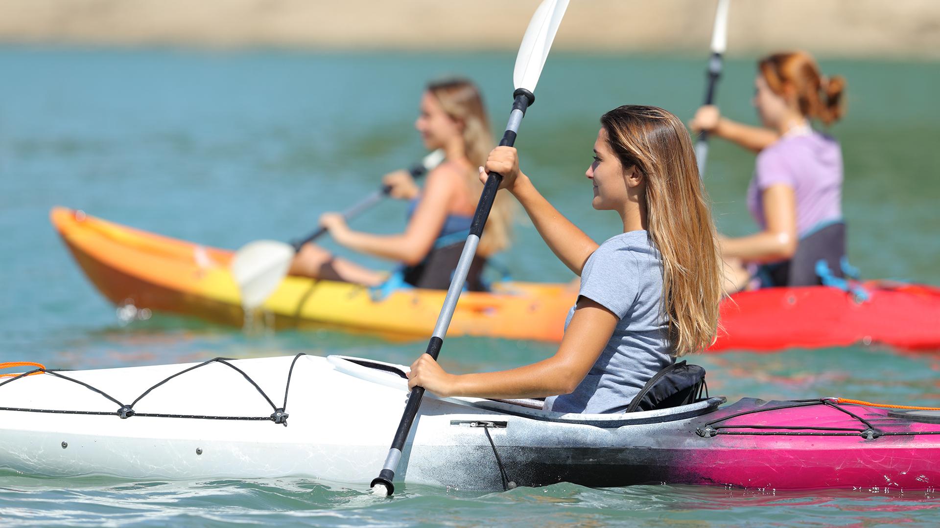 A group of women kayaking on the water, paddling together under a clear sky with calm surroundings