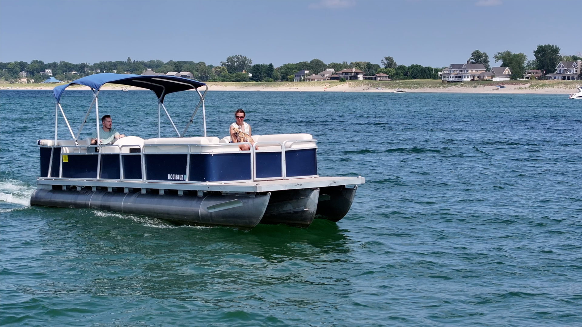 A man driving a pontoon boat on Lake Michigan with his wife and her service dog
