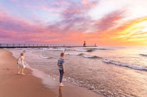 Two children on the beach at sunset with the St. Joseph Lighthouse in the distance.