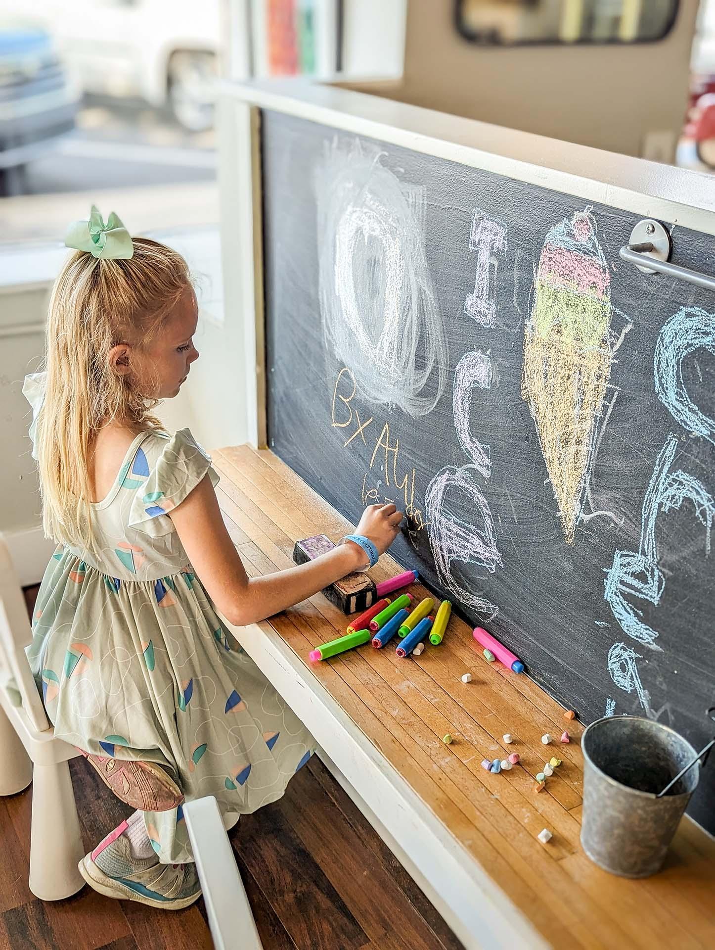 A child drawing a picture of ice cream on a chalk board. 