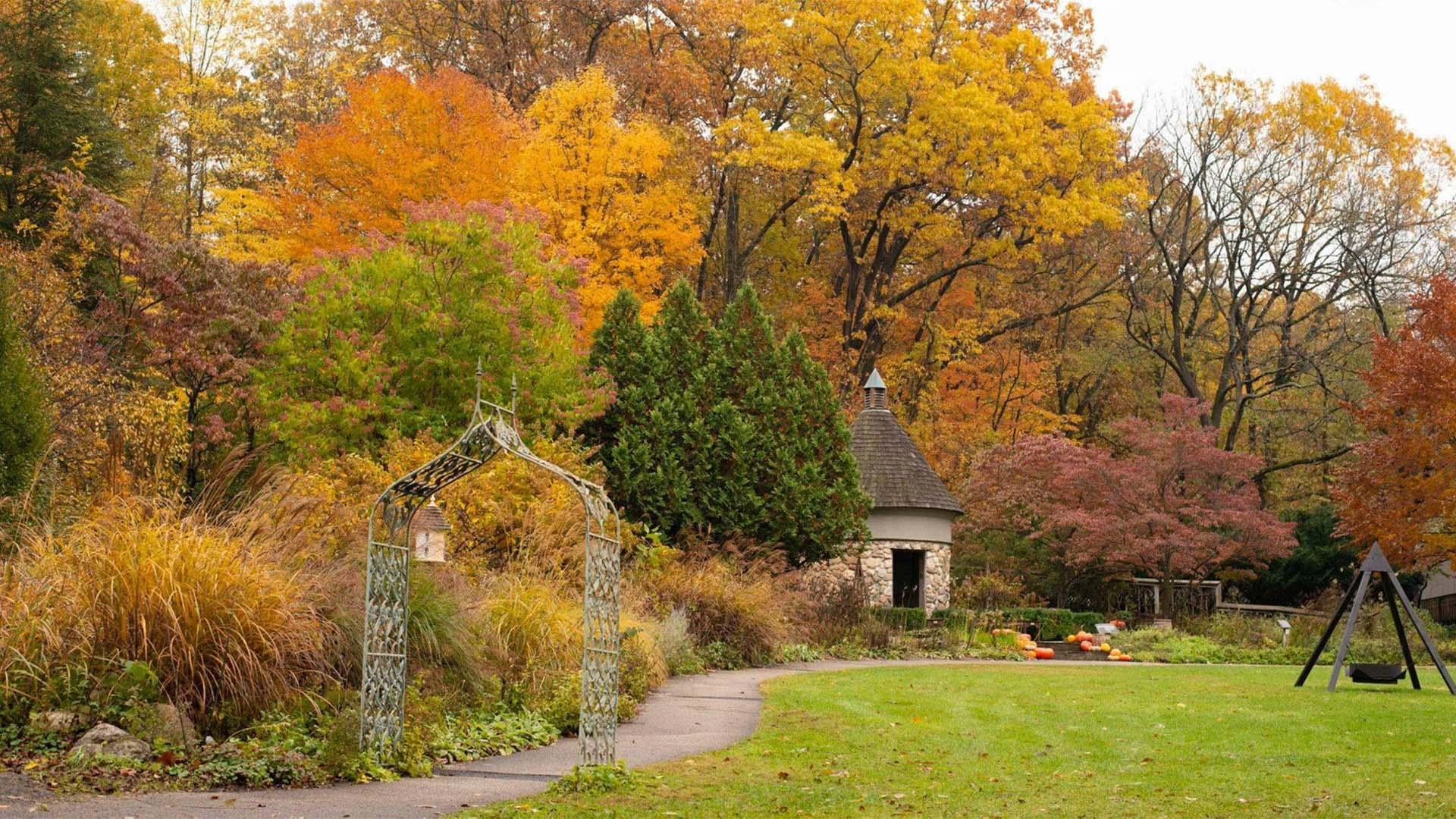 Scenic garden view with vibrant fall foliage, stone cottage, and winding path at Fernwood Botanical Garden and Nature Preserve.