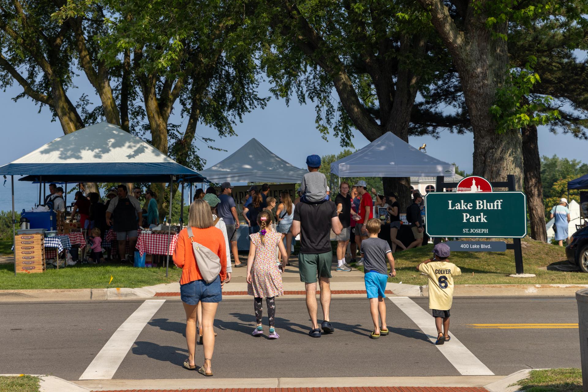 A family walking towards the Farmers Market on a Saturday in Downtown St. Joe, the sign 
