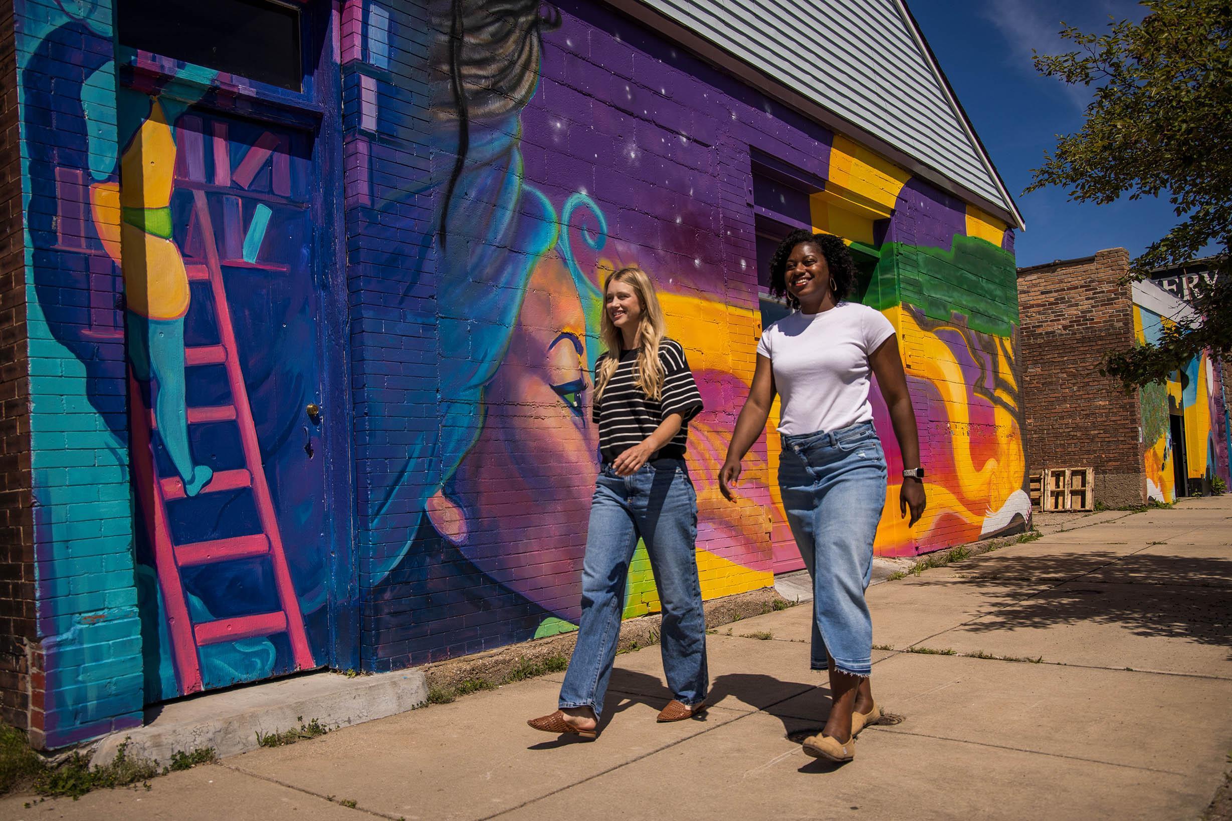 Two people walking past the The Livery “Continued Legacy” mural.