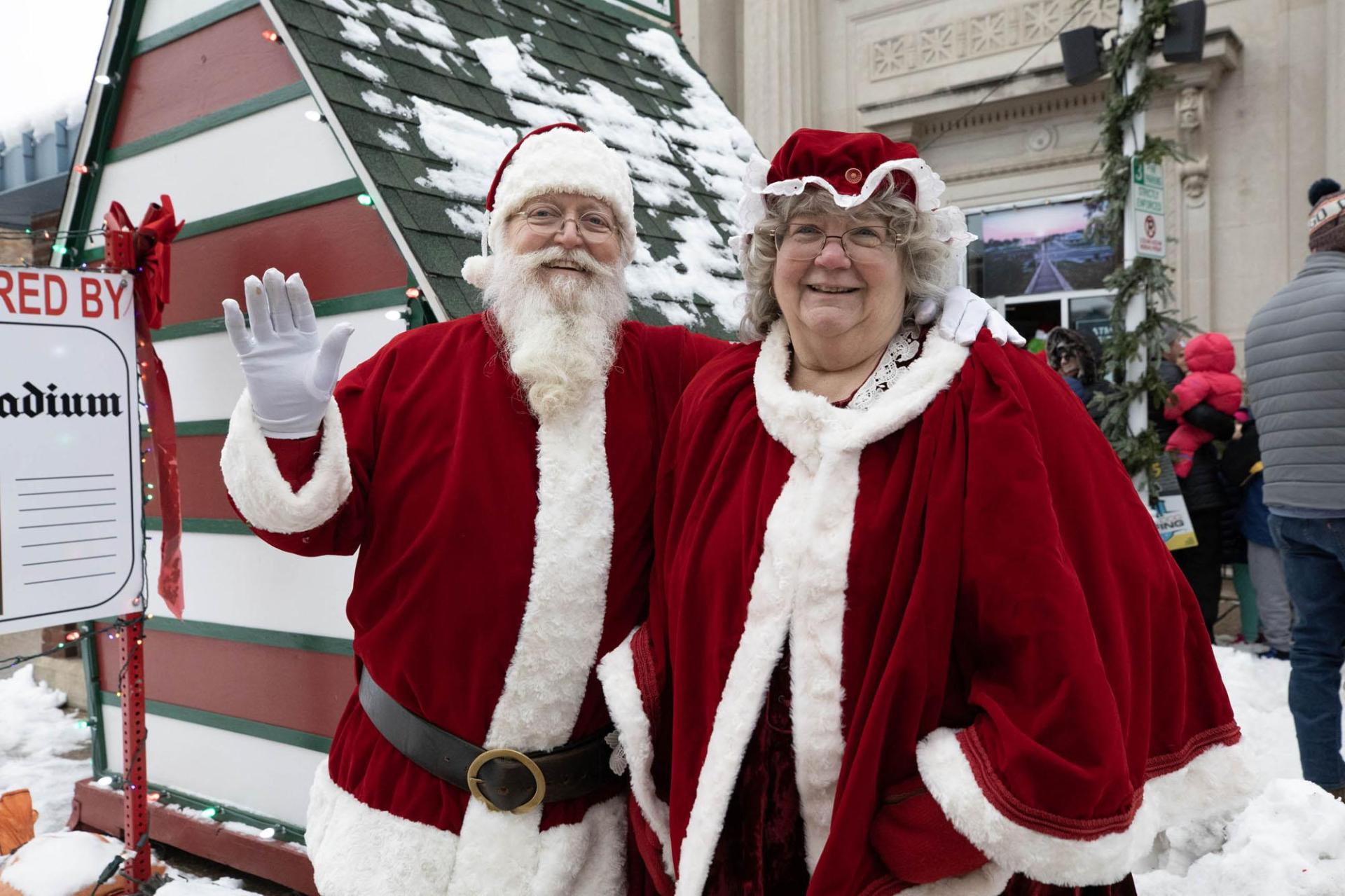 Mr. and Mrs. Claus pose cheerfully in front of Santa’s house.