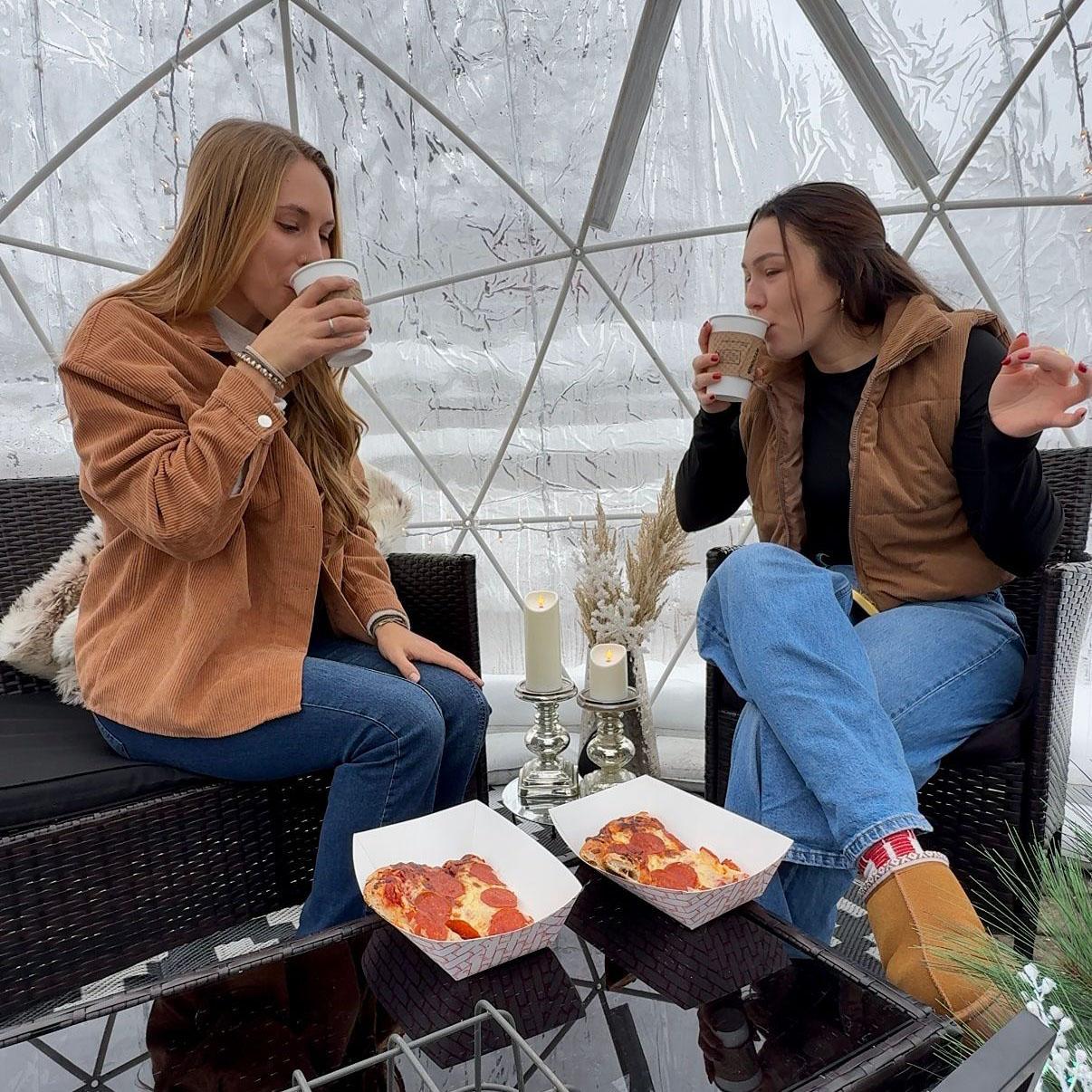 Two people enjoy drinks and pizza inside an outdoor igloo at Round Barn Winery.