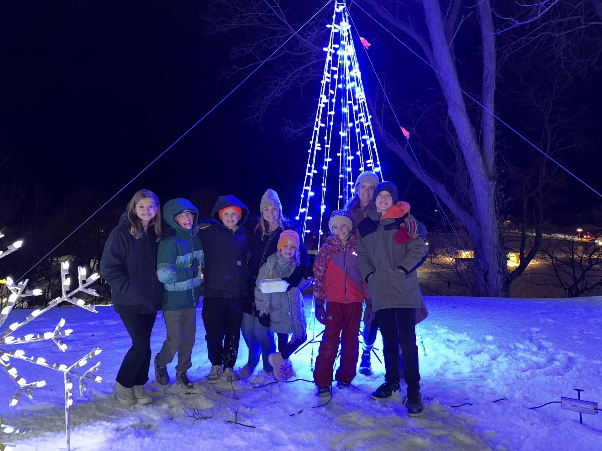 A group of people pose for a photo with holiday lights in the background.