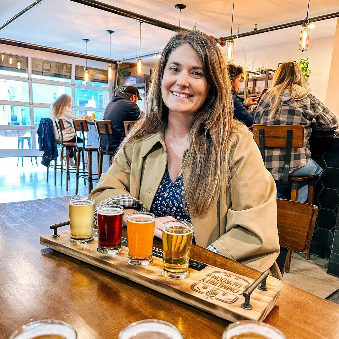 A person poses for a photo with a flight of beer at The Community Tap.