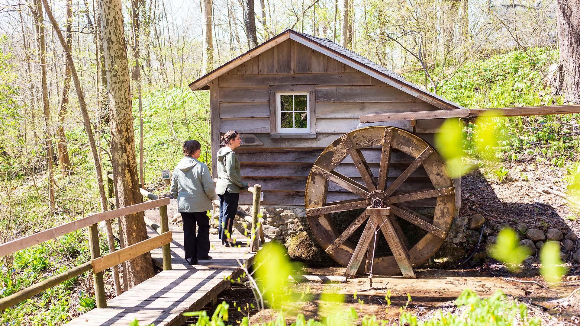 Two people walking past the waterwheel at Fernwood Botanical Garden and Nature Preserve.