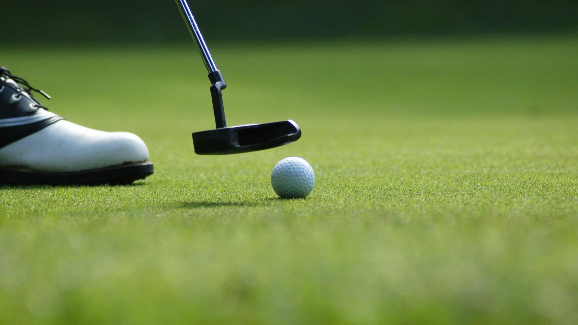 A close-up of a golf club behind the ball as a golfer prepares to make a putt.