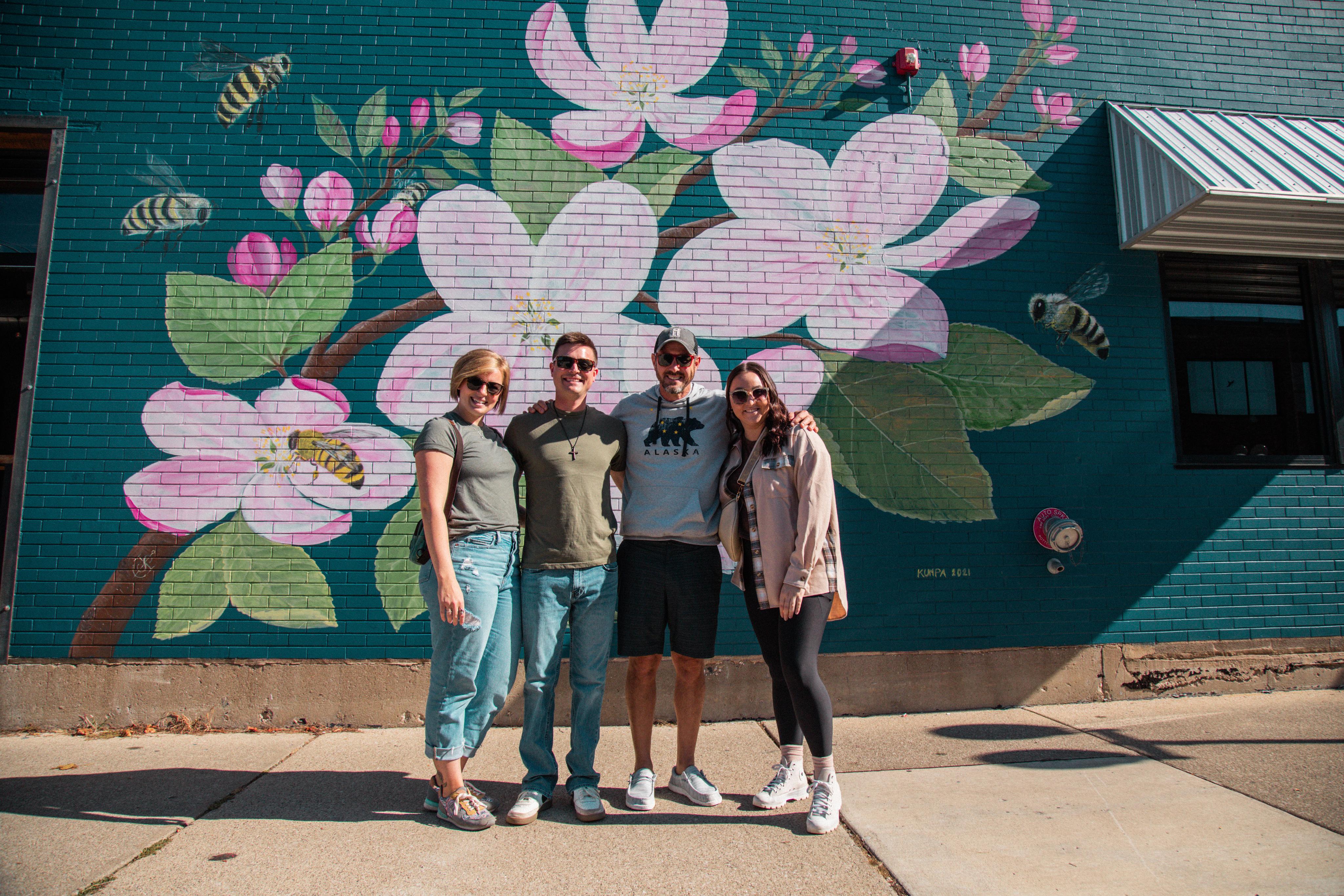 A group stands in front of a mural of flowers and bees at Silver Harbor Brewing Company.