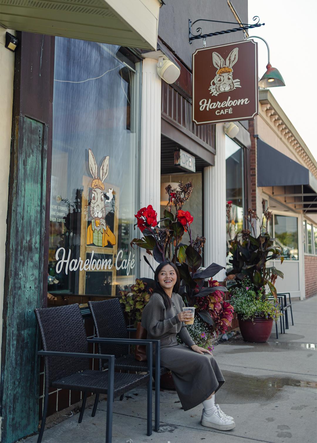 A woman smiles while sitting outside Hareloom Café, holding a drink