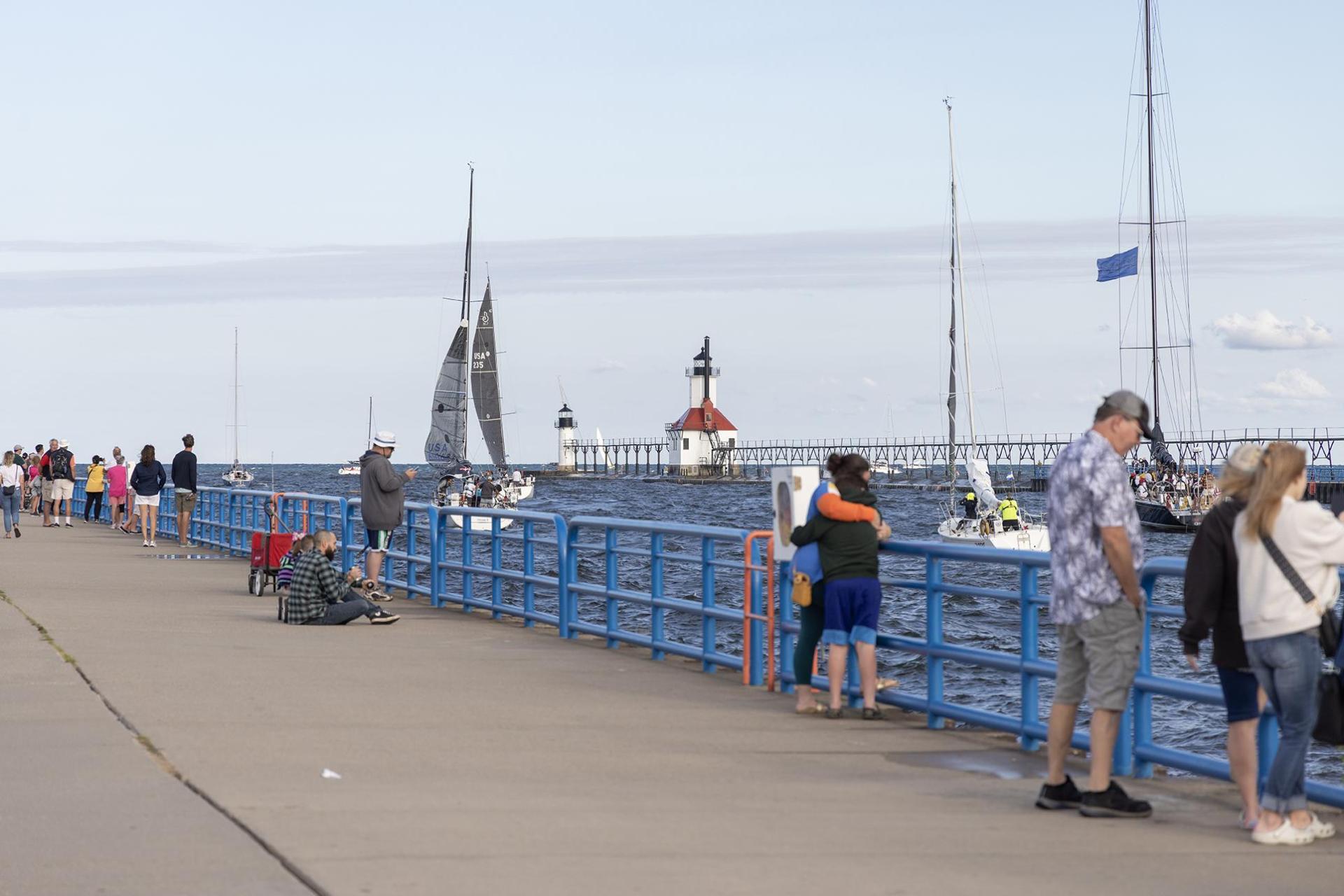 A view of the north and south piers, with the lighthouse, sailboats, and crowds of people walking along the pier.