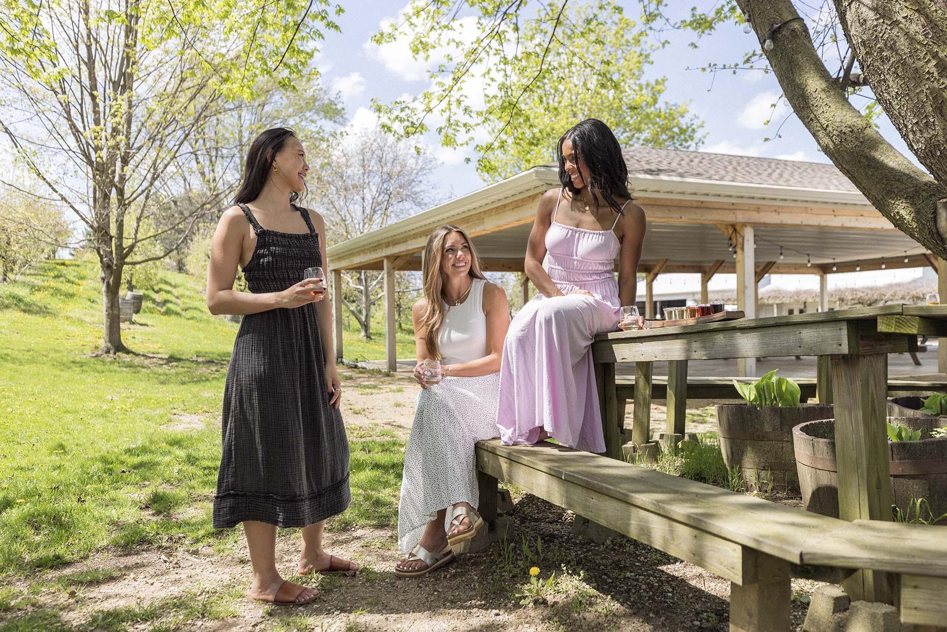 Three women enjoy glasses of wine outdoors on a sunny day at Lemon Creek Winery.