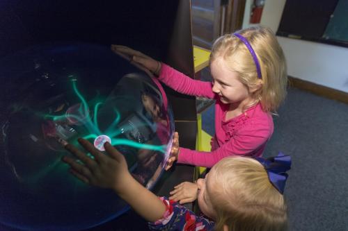 Two kids interact with a glowing plasma globe.