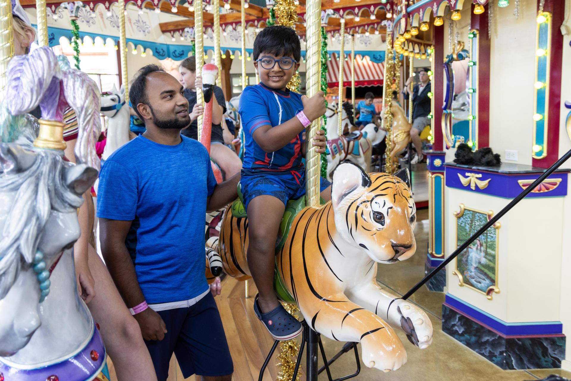 A child rides the tiger at Silver Beach Carousel while his father stands beside him.