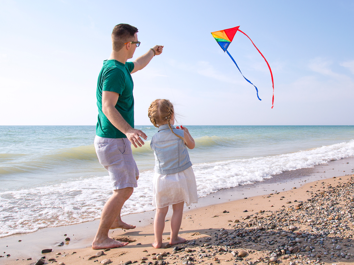 A father helping his young daughter fly a kite on the beach, with Lake Michigan and a clear_Ufjk