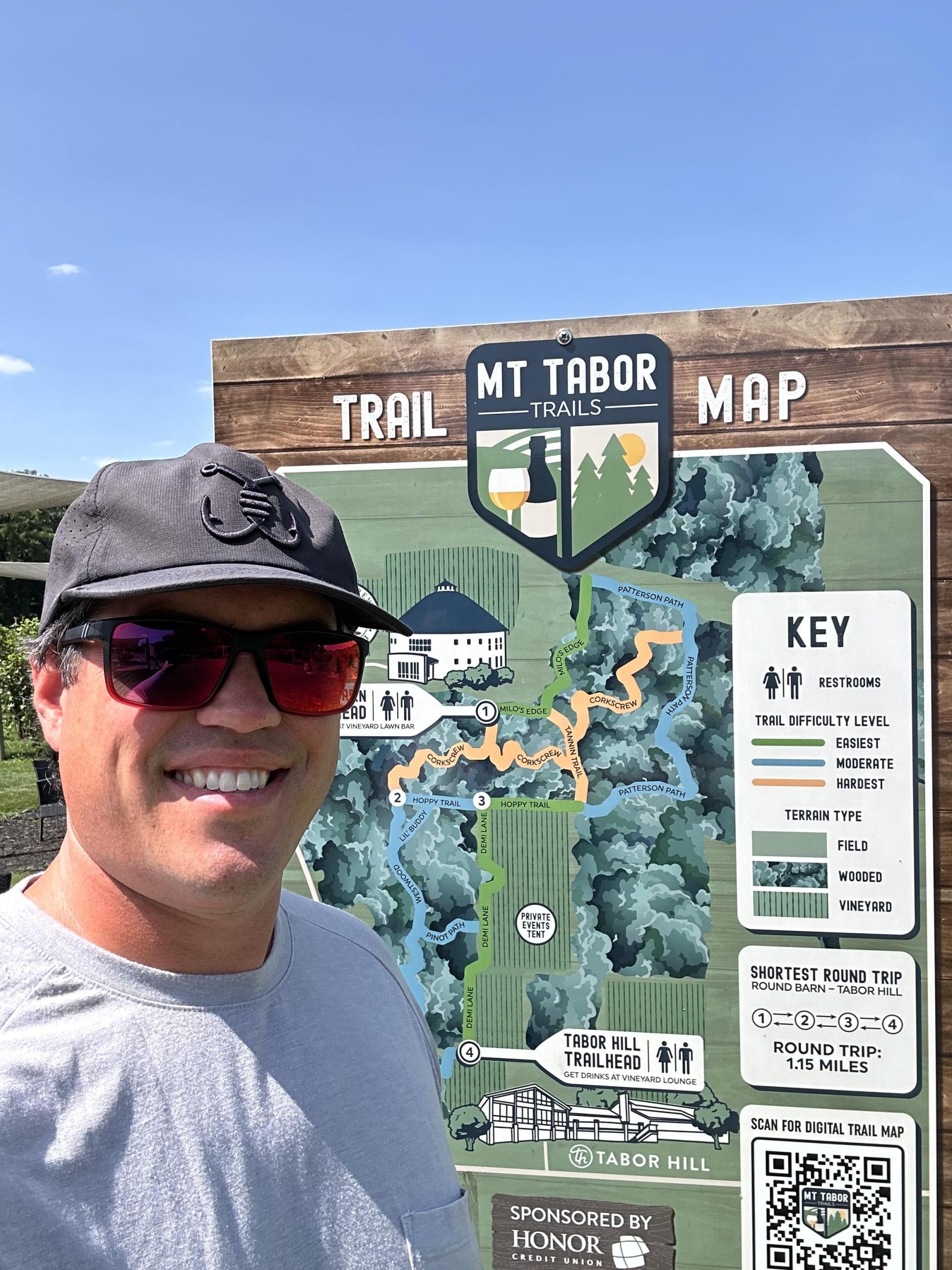 A person taking a selfie in front of the Mt. Tabor Trail map. 