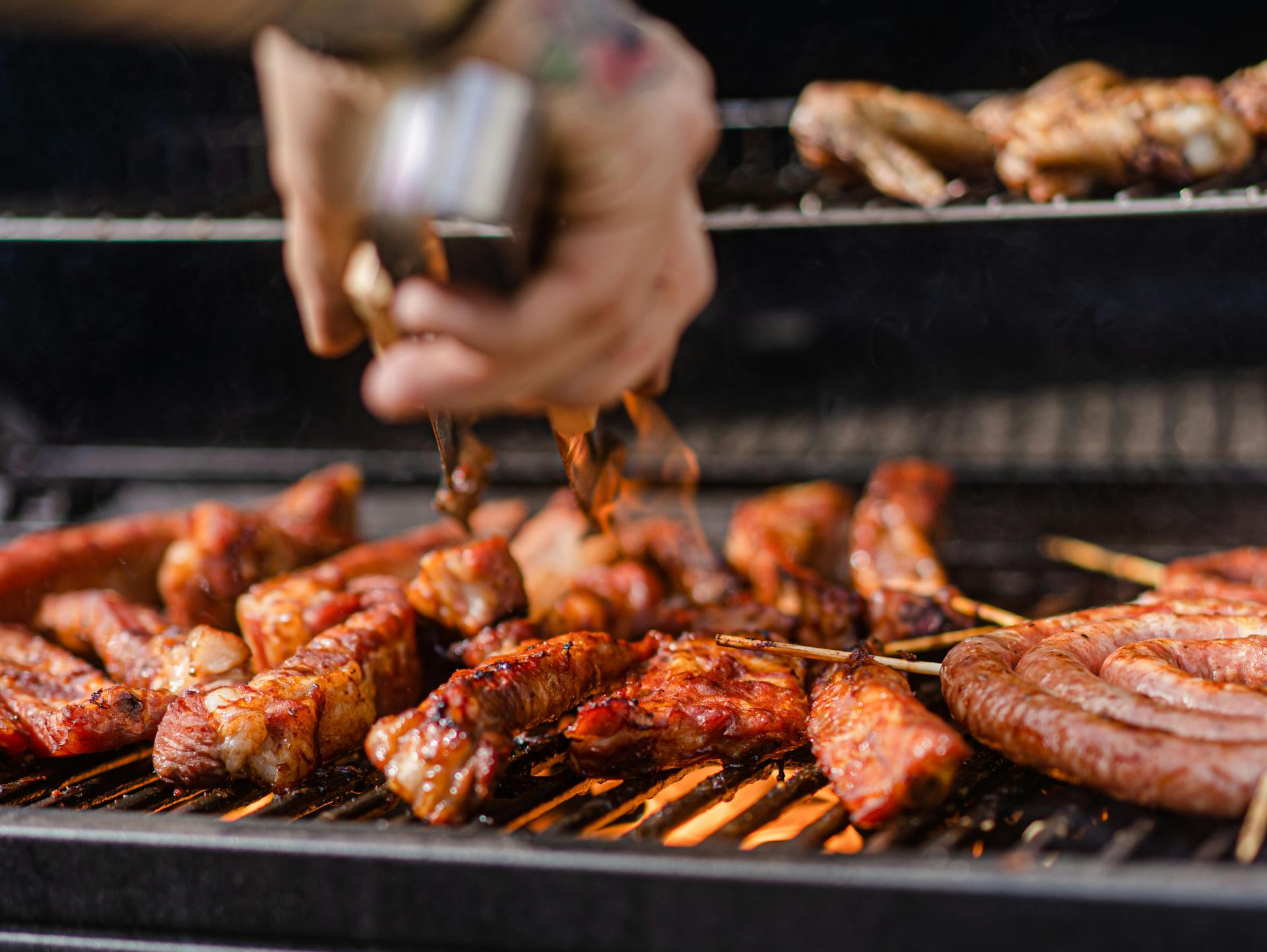 A grill filled with sizzling meat as someone flips food with a pair of tongs.
