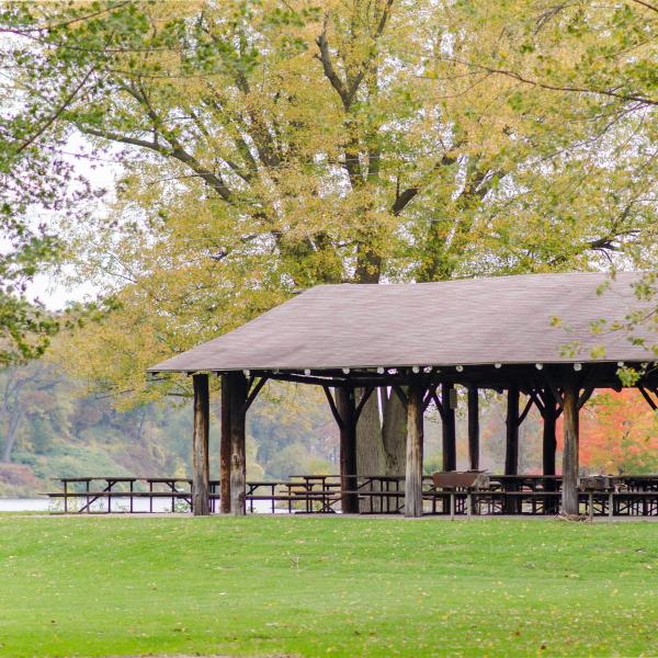 View of a park pavilion with a big tree behind it and fence, river in the background