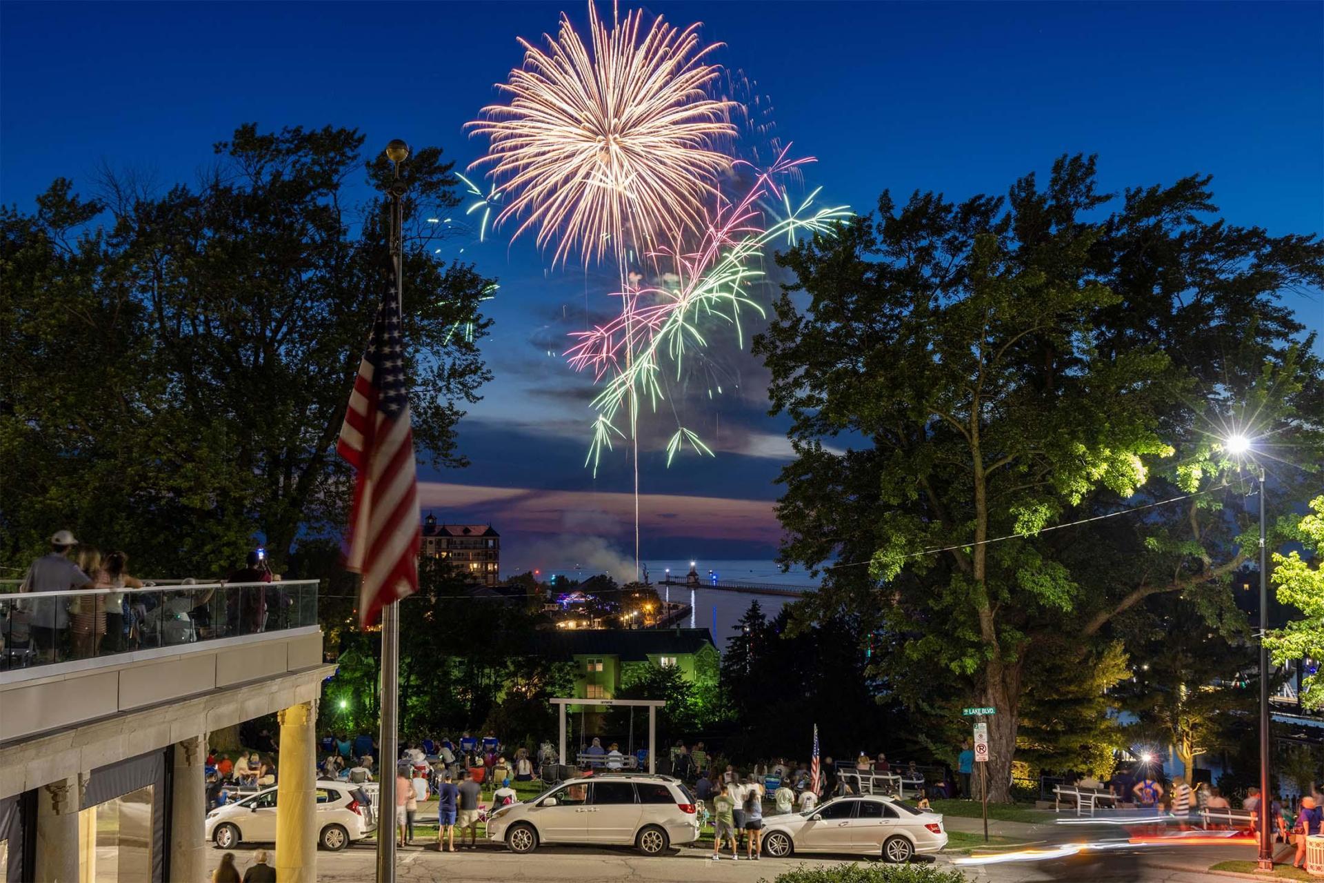 Fireworks light up the sky above St. Joseph, with the bluff, lighthouse, and Lake Michigan in view.