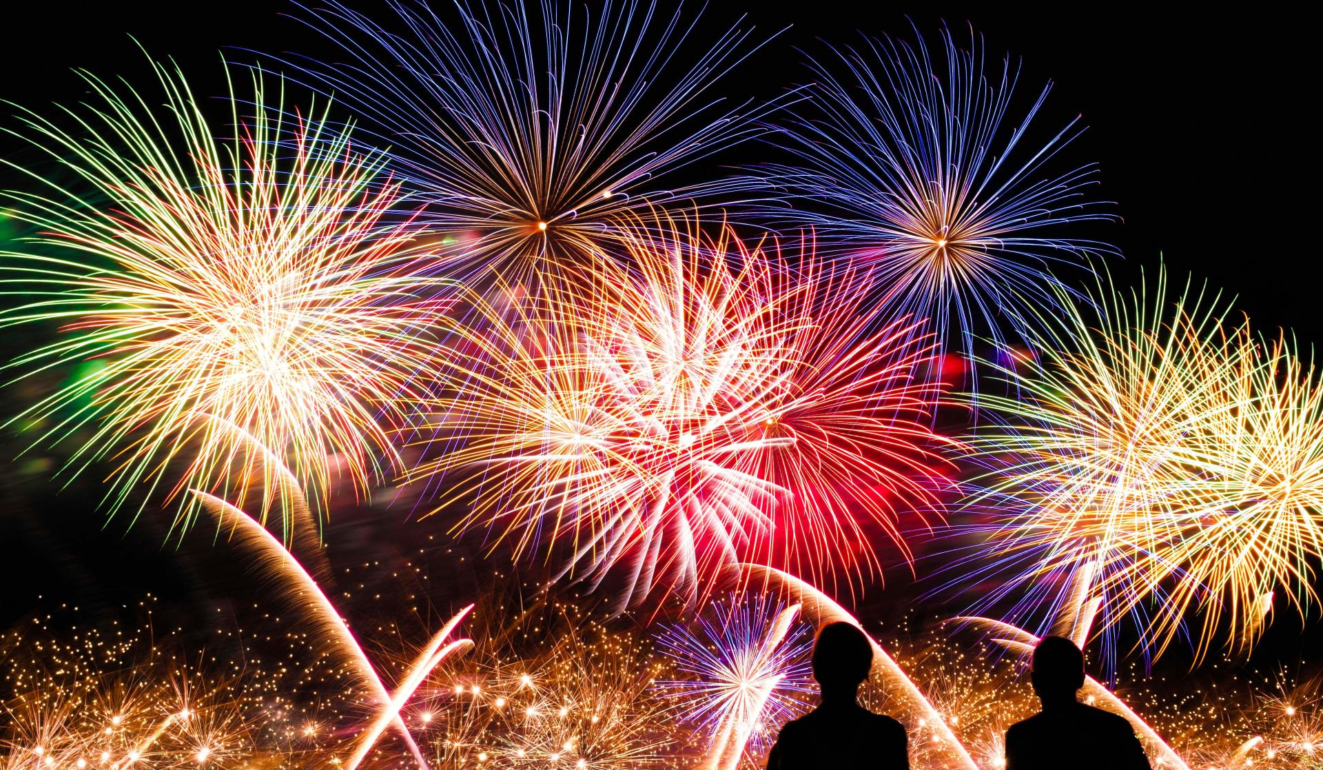 Two people watch a colorful fireworks display illuminate the night sky.
