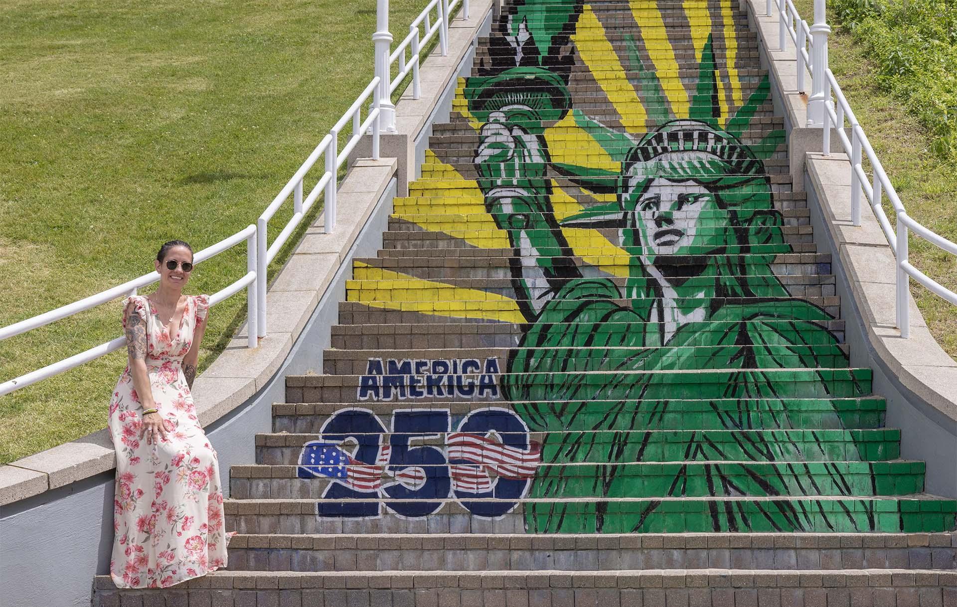 Artist Kimberly Wood poses beside the America 250 mural on the Bluff Steps in St. Joseph, Michigan.