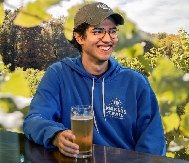 Man holding a beer smiling while wearing the MT blue hoodie for 2026 rewards