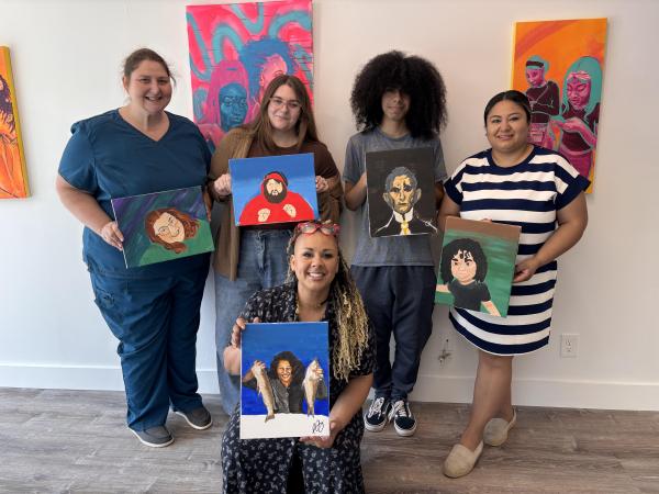 Group of people holding paintings while smiling.