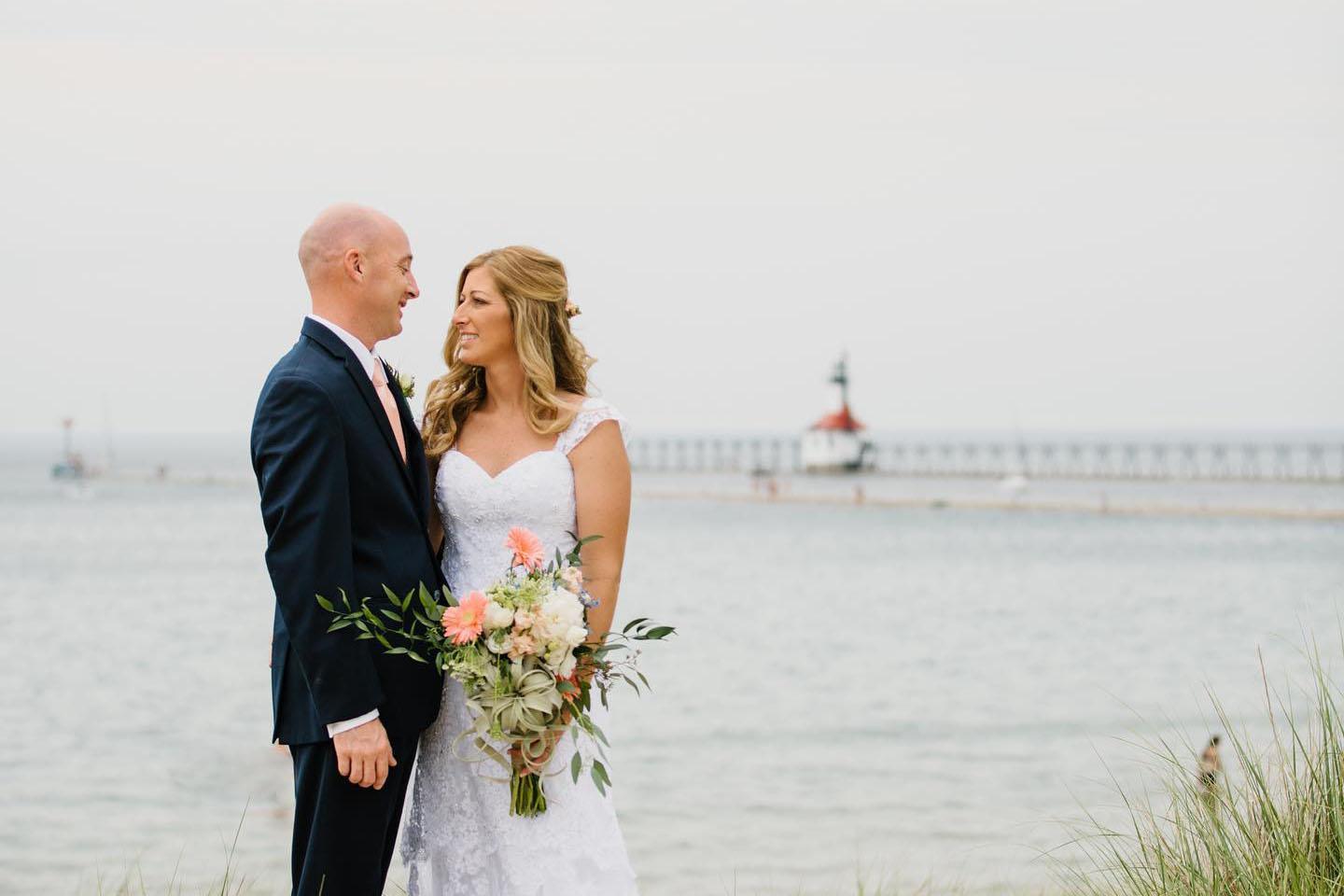 A couple posing for a photo on the beach with the lighthouse in the distance. 