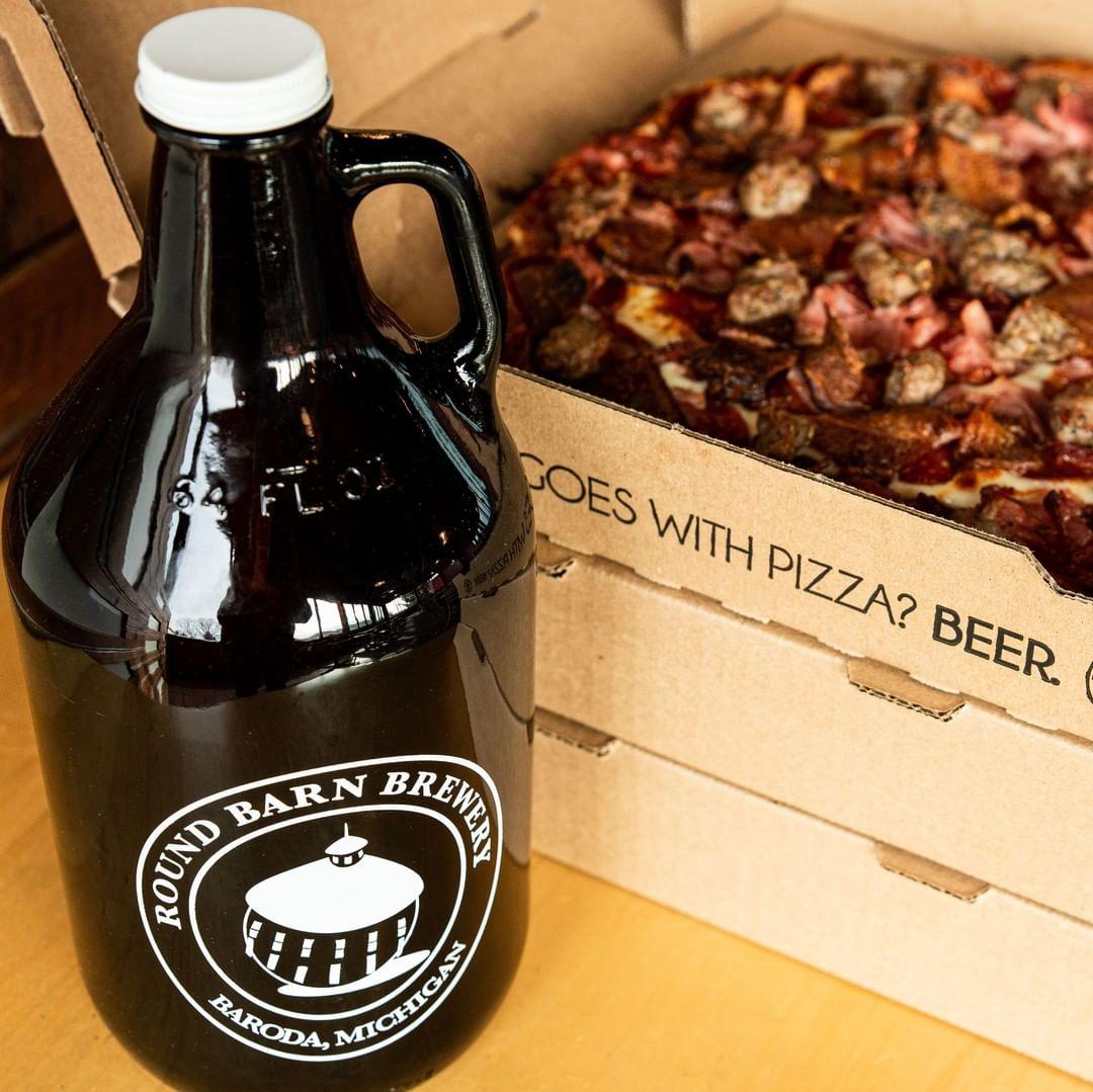 An open box of pizza with a growler of beer