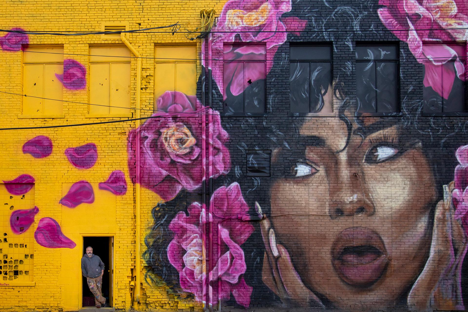 A man standing next to a mural of a woman and flowers