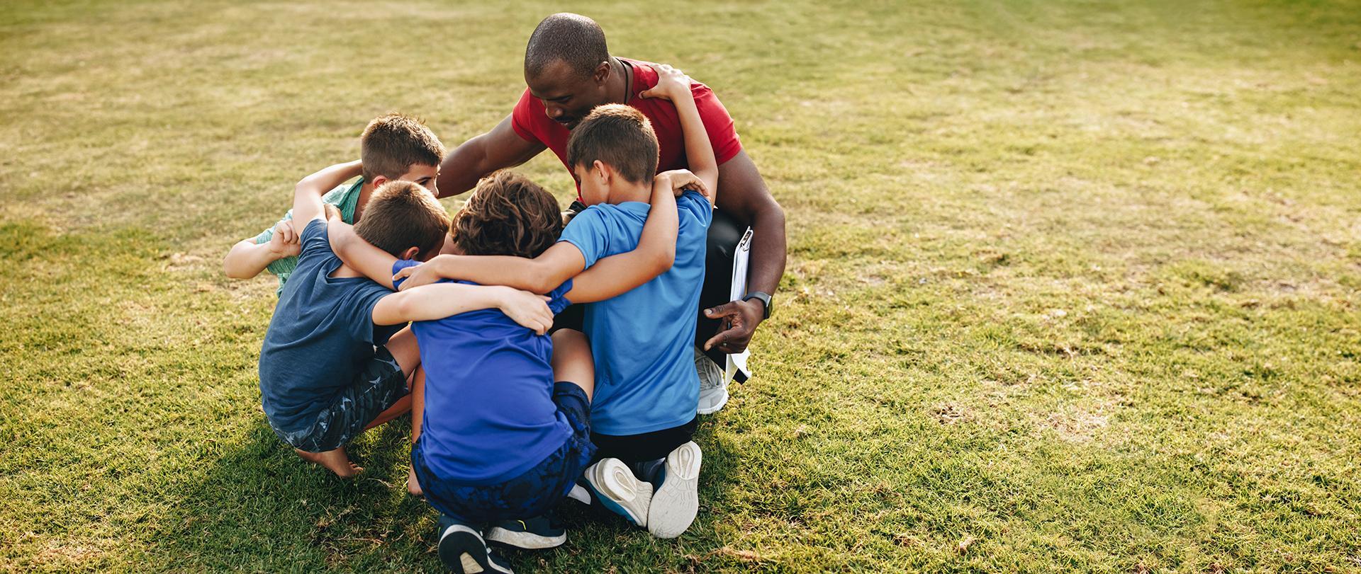 group of children with a coach in a circle on a field 