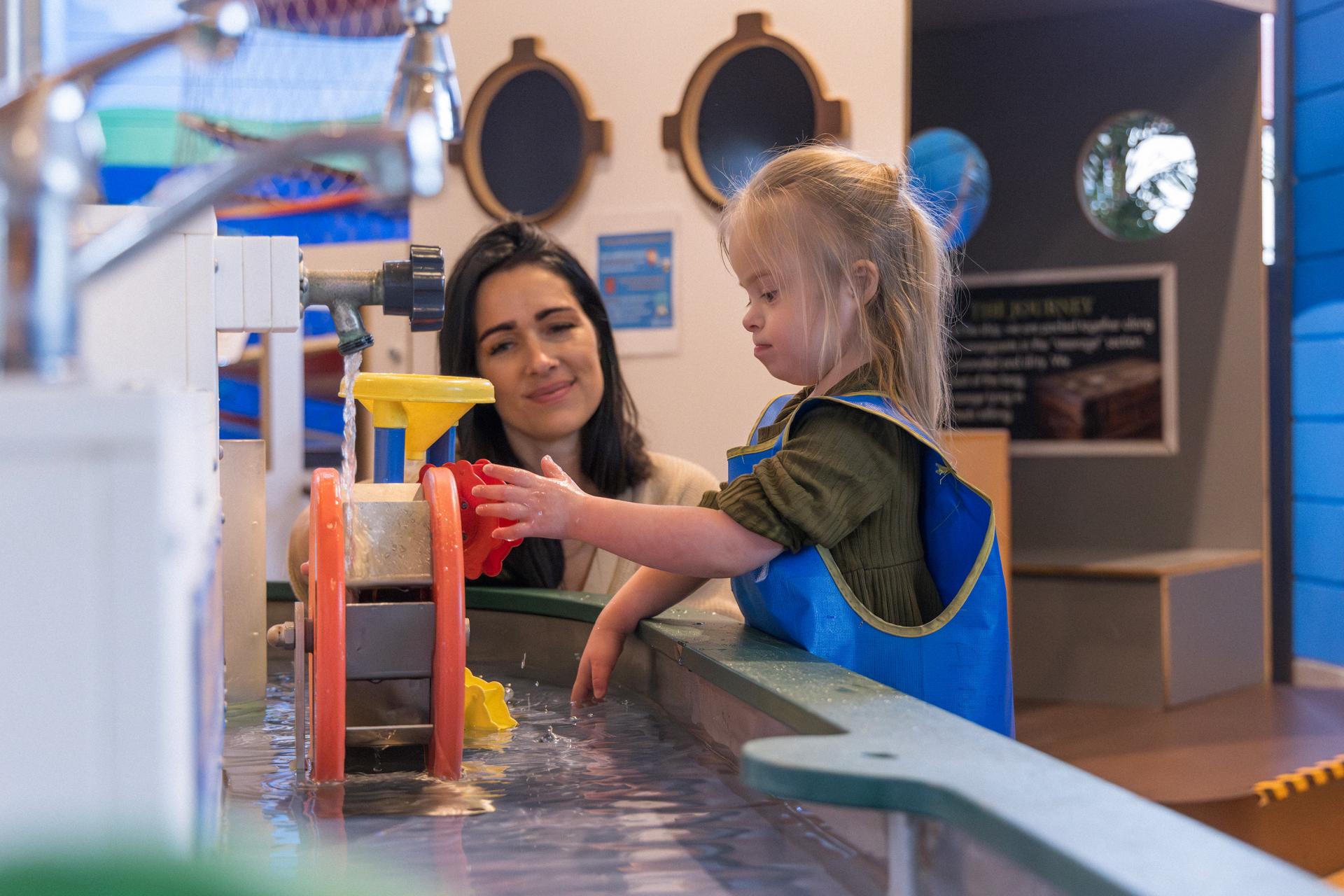 a mother and daughter playing at the water table located in the discovery zone