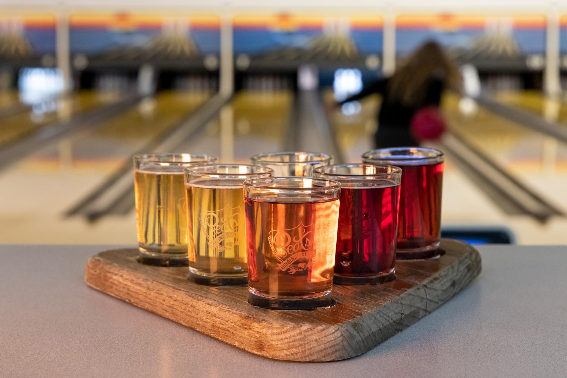 A tasting tray of hard ciders and a woman bowling at Peat