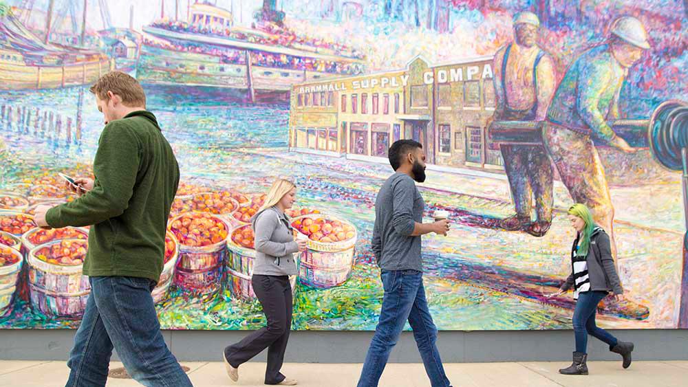 people walking in front of a colorful mural of benton harbors golden age