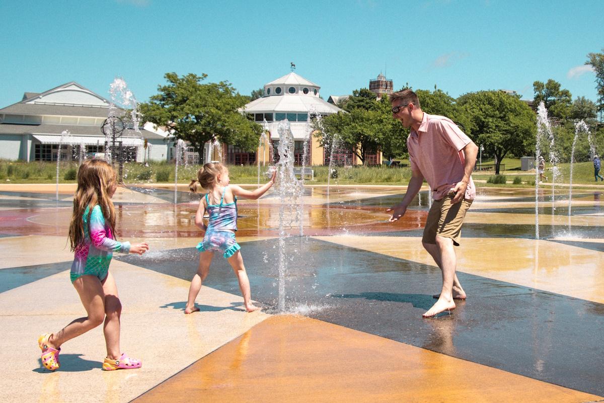 a dad playing with two young children at the whirlpool compass fountain