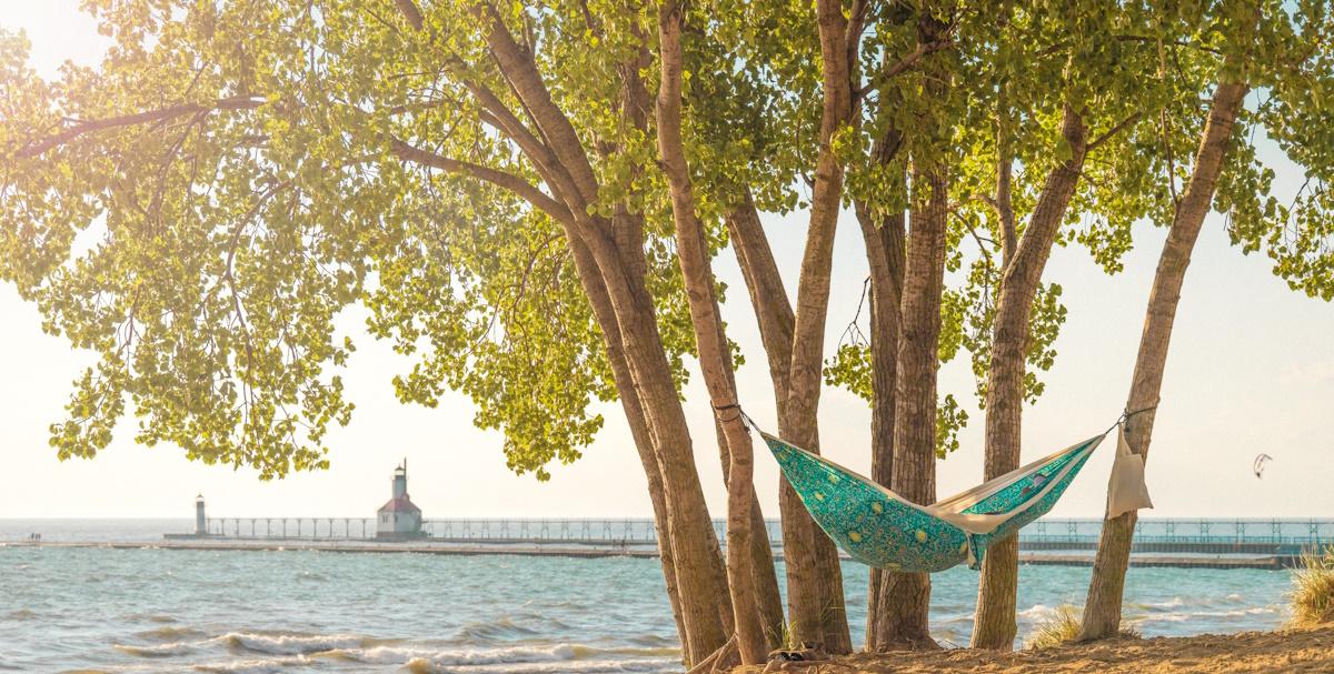 a hammock between trees at silver beach park with the lighthouse in the background