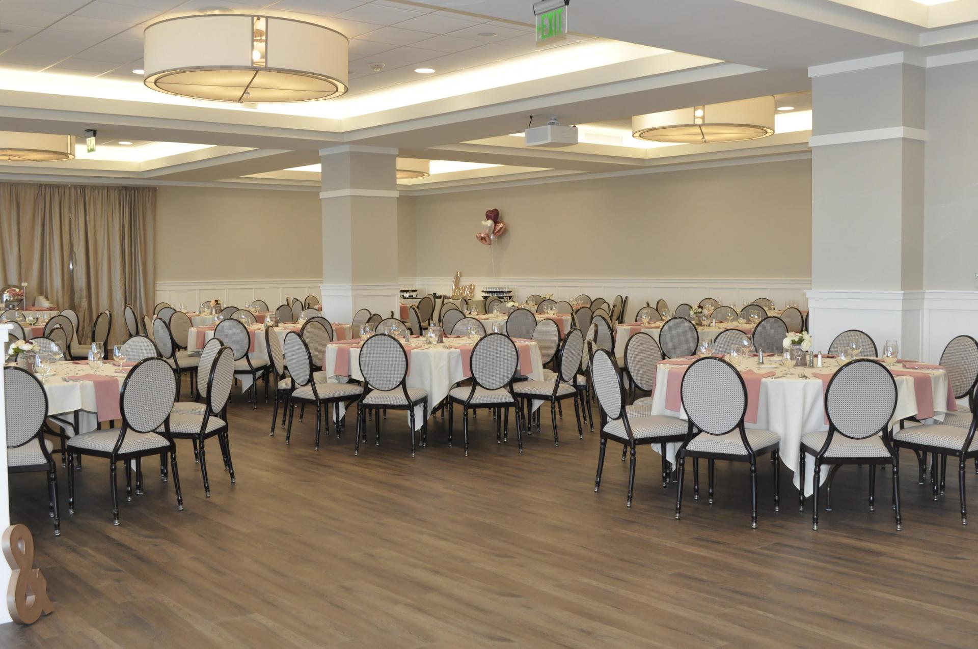 Ballroom set up for a wedding or dining event, featuring elegantly arranged tables, floral centerpieces, and ambient lighting.