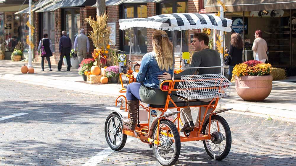 A couple riding a surrey bike in downtown St. Joseph Michigan.