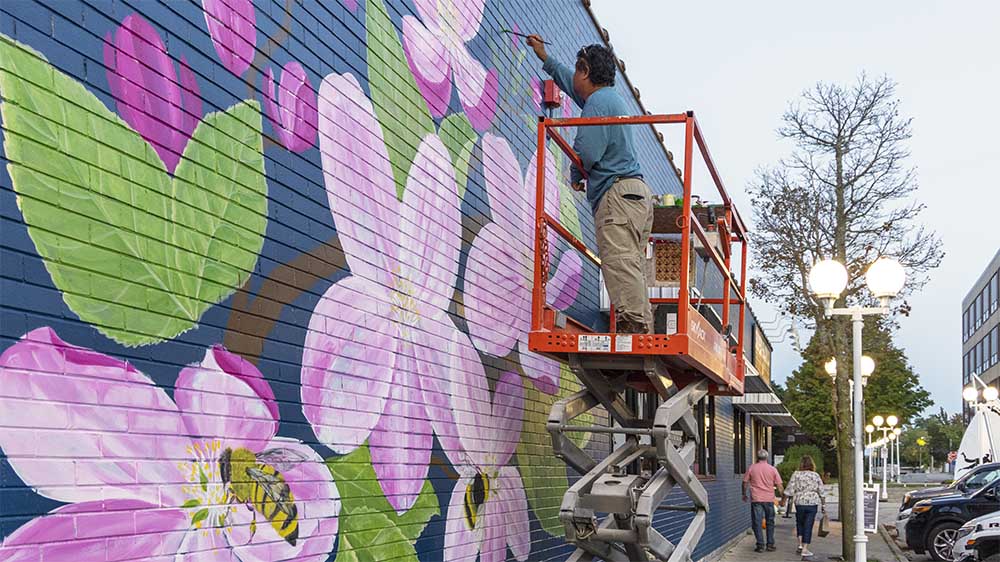 Artist Kumpa working on a mural featuring flowers and bees.