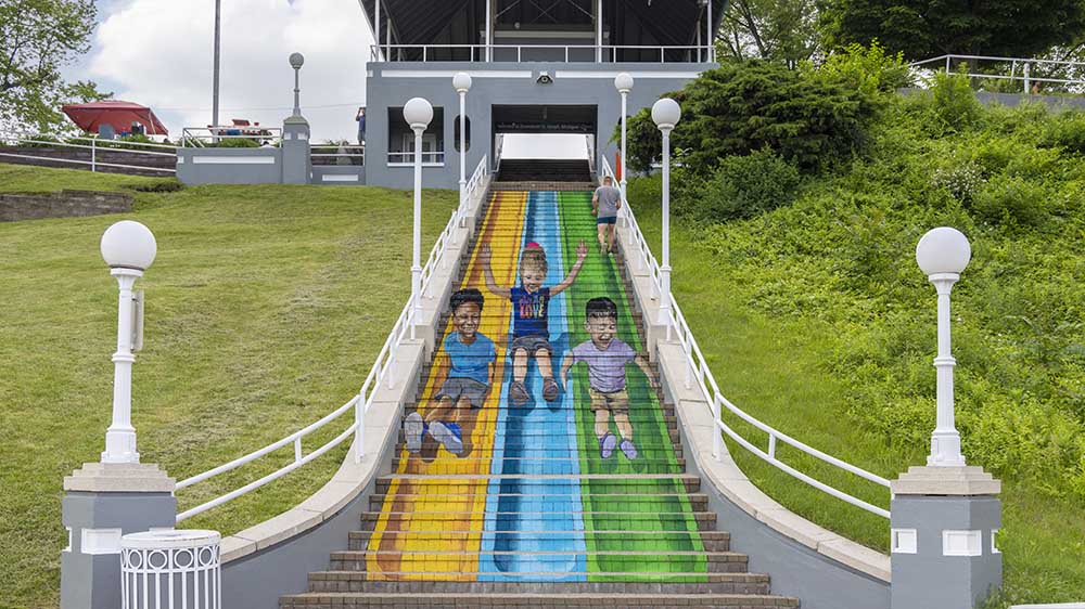 Mural on the bluff staircase in St. Joseph showing kids sliding. 
