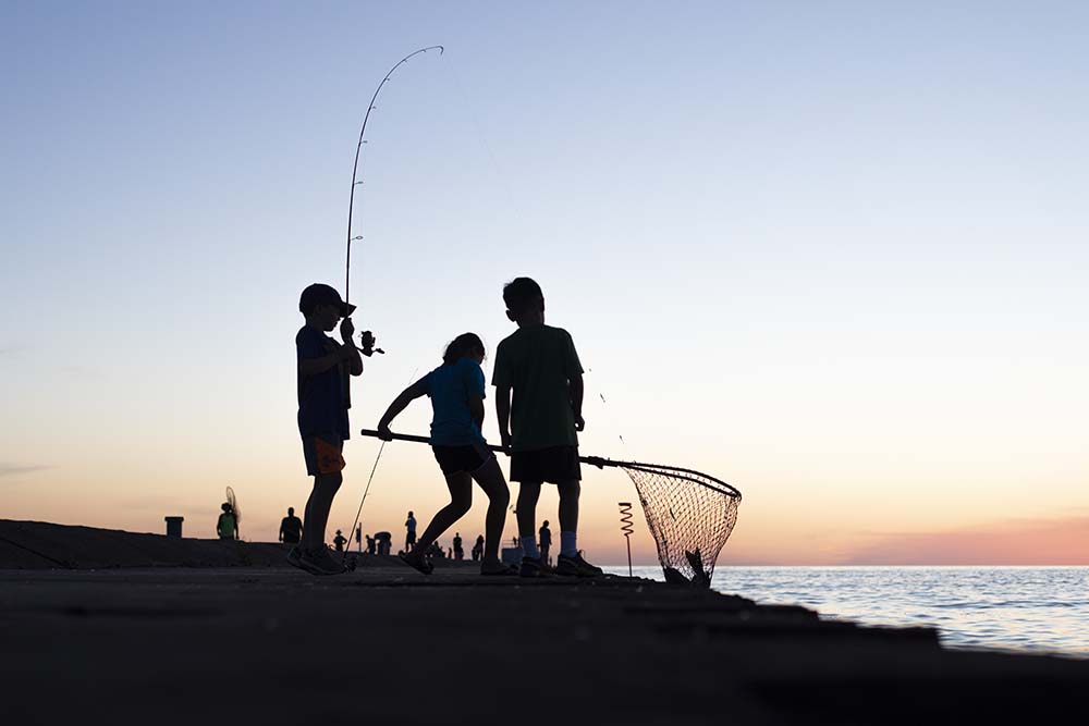 Three young people fishing from the pier in St Joseph.