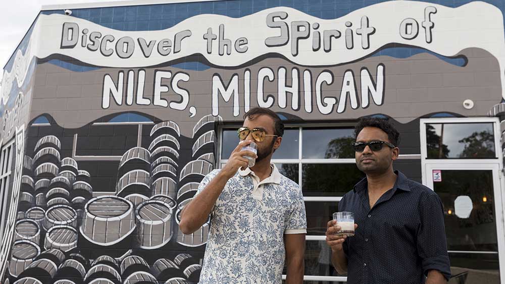 Two people with drinks standing by the mural at Iron Shoe.